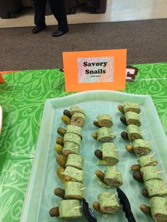 an assortment of food is displayed on a table with people standing in the background looking at it