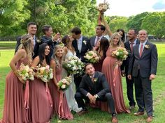 a group of people standing around each other in front of some trees and grass with one person holding up a trophy