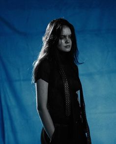 a woman standing in front of a blue backdrop with her hands on her hips and looking off to the side