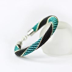 a bracelet with black and teal beads on a white background is seen in this image