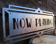 a metal sign that says now playing on the side of a wooden wall next to a barrel