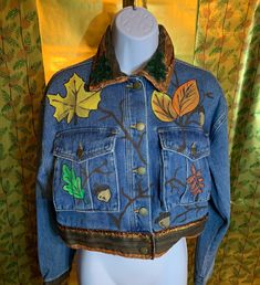 Autumn Leaf is a hand painted jean jacket.  It is decorated with different color leaves.  Collar, sleeves and hem are embellished with a brown and orange trims.  One line of trim is orange and brown shimmering lace.  On the collar are two 1960's leaf appliques.  A beautiful addition to any fall wardrobe. Hippie Cotton Denim Jacket For Fall, Fitted Retro Denim Jacket For Fall, Hand Painted Multicolor Outerwear For Fall, Multicolor Hand Painted Outerwear For Fall, Hippie Denim Jacket For Fall, Hippie Brown Outerwear For Fall, Embroidered Multicolor Denim Jacket For Fall, Hippie Fall Festival Denim Jacket, Hand Painted Long Sleeve Denim Jacket For Fall