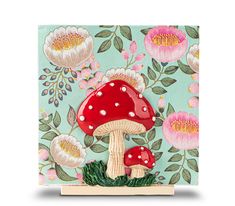 a red mushroom sitting on top of a wooden block with flowers and leaves around it