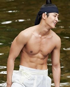 a shirtless man standing in the water wearing white shorts and a black headband