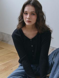 a young woman sitting on the floor wearing jeans and a black cardigan sweater is looking at the camera