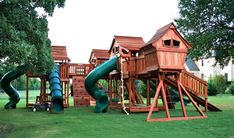 a wooden play set in the middle of a green yard with slide and climbing frame