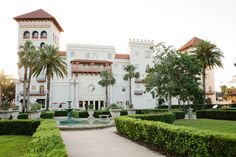 a large white building sitting next to a lush green park filled with trees and bushes