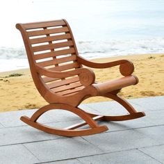 a wooden rocking chair sitting on top of a cement floor next to the ocean and sand