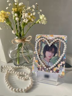 a vase filled with flowers next to a heart shaped photo frame and pearl necklace on a table