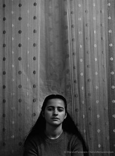 black and white photograph of a woman with long hair sitting in front of a curtain