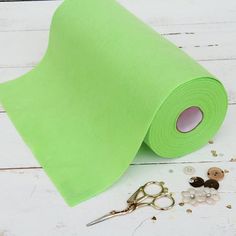 a roll of green paper next to scissors and buttons