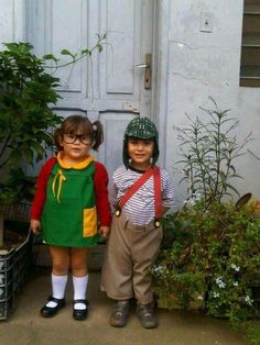 two young children standing next to each other in front of a white door with potted plants