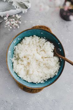 a blue bowl filled with white rice next to a wooden spoon on top of a table