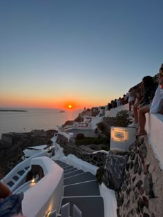 people are sitting on the edge of a cliff watching the sun rise over the ocean