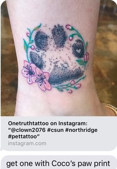 a dog paw tattoo on the ankle with pink flowers and green leaves around it's paws