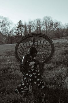 a woman sitting on top of a wicker chair in the middle of a field