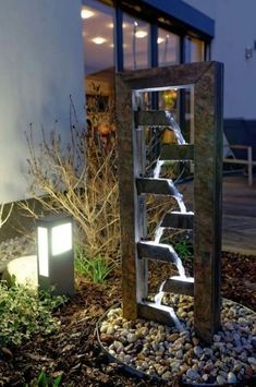 a water fountain in the middle of a garden at night with lights shining on it