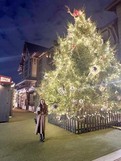 a woman is standing in front of a christmas tree at night with lights on it