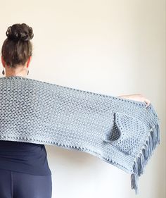 a woman is holding up a knitted shawl