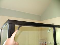 a person pointing to the top of a microwave oven in a room with white walls