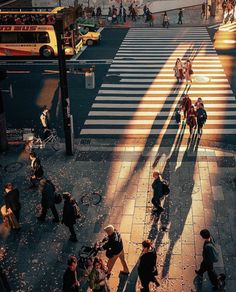 people crossing the street at an intersection with their shadows on the ground