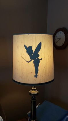 a lamp that has a tinkerbell on it with a clock in the background