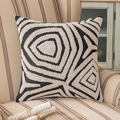 a black and white pillow sitting on top of a couch next to a chair with pillows