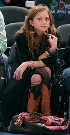 a woman sitting on the floor with her hand in her mouth and wearing cowboy boots