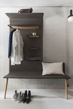 a coat rack with shoes and clothes on it in a white tiled room next to a lamp