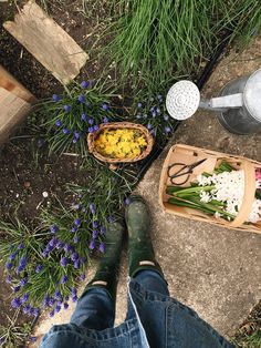 a person standing next to a basket filled with flowers and cutting utensils on the ground