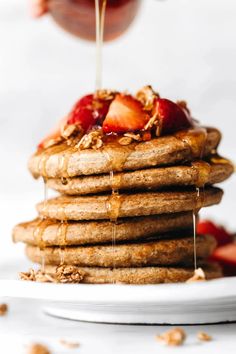 a stack of pancakes with syrup being drizzled over them and topped with strawberries