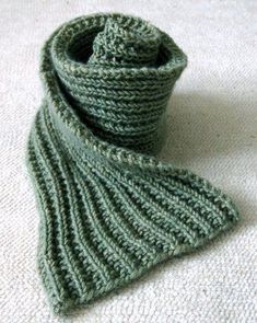 a green knitted scarf sitting on top of a white blanket