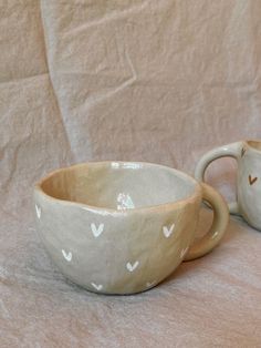 two ceramic cups sitting on top of a white cloth covered table next to each other