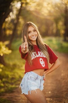 a beautiful young woman giving the peace sign while standing on a dirt road with trees in the background