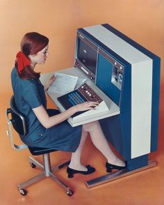 a woman sitting at a desk with a laptop computer in front of an old fashioned machine