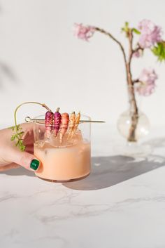 a hand holding a drink with strawberries on the rim and garnished with flowers