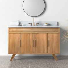 a bathroom vanity with two sinks and a round mirror on the wall next to a potted plant