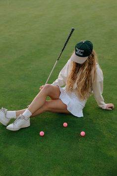 a woman sitting on the ground with a golf club and ball in her hand,