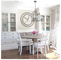 a dining room table with white chairs and a clock on the wall above it's doors