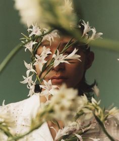 a woman with white flowers in her hair and eyes looking at the camera while she is surrounded by greenery