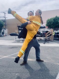 a man and woman dressed in yellow are dancing on the street with one leg up