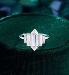 an emerald colored diamond ring sitting on top of a green velvet bag