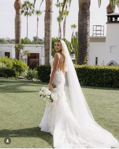 a beautiful woman in a wedding dress standing on the grass with palm trees behind her