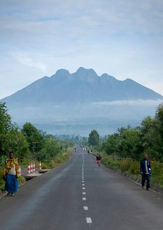 two people walking down the middle of an empty road with a mountain in the background