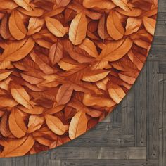 an oval shaped rug with orange leaves on the floor in front of wood planks