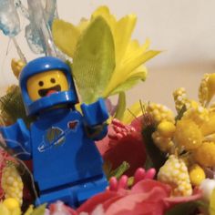 a lego man standing in front of flowers and corn on the cob with his hand up