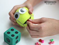 a child is playing with a green ball and two dices that have eyes on them