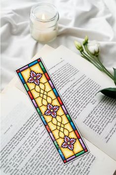 a stained glass bookmark sitting on top of an open book next to a candle