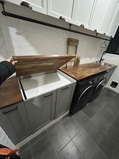 a woman standing next to a washer and dryer in a room with white cabinets