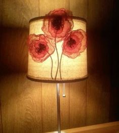 a lamp with red flowers on it sitting on a table next to a wooden wall